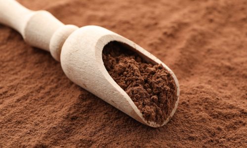 Wooden scoop and cocoa powder background, close up
